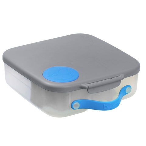 A square, transparent plastic B.Box Lunch Box with a gray lid and leak-proof silicone seals is shown. The lid features a small blue circular latch and a matching blue handle. The handle is attached to the front of this B.Box lunchbox for easy carrying.