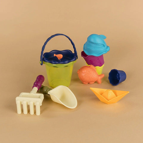 A collection of vibrant beach toys is arranged on a beige surface. It features a green bucket with a blue handle, a yellow rake, a white scoop, a blue and purple whale mold, an orange fish mold, a purple shell mold, and a yellow toy boat—all ideal for filling your Battat Beach Wagon with Toys by Battat or crafting exquisite sandcastles.