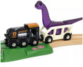 The Brio World Dinosaur Adventure Set, by Brio, features a black engine with an orange top that pulls a white car transporting a purple, long-necked dinosaur. The train runs on a curved wooden track embellished with green and pink flower details.