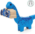 A blue, cartoon-style, wooden dinosaur toy with dark blue spots holds a smaller wooden piece shaped like its mouth, featuring eyes and circular patterns. A magnet icon in the top right corner hints at magnetic components, making it perfect for any Brio World setup or to complement the Brio World Dinosaur Battery Train.