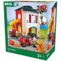 The image showcases the Brio World Fire Station by Brio, a toy set designed for children aged 3 and above. This set includes a fire station complete with two fire trucks, a firefighter figurine, a building with a yellow slide, and a pretend fire. The packaging features the toy along with illustrations of various play scenarios.