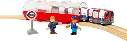 The Brio World London Underground Train, part of Brio's Trains of the World series, features a miniature model of the London Underground. It includes two figurines—one in a suit and the other in a uniform—standing near the platform. The track and train cars display iconic red and blue colors, along with an Underground sign.