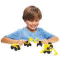 A child with brown hair wearing a blue shirt is playing with the CAT Little Machines 5 Pack, which includes miniature construction vehicles like a yellow dump truck, front loader, and excavator, on a white background. Smiling brightly, the child fully immerses in role-playing and appears to be enjoying the playtime.