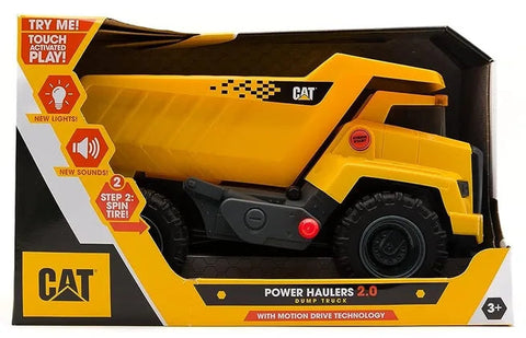 A yellow CAT Power Haulers - Dump Truck is displayed in a box with "Try Me!" instructions. Featuring new lights, sounds, and spin tire action for interactive play, this truck is designed for children aged 3 and up. The box highlights its advanced Motion Drive Technology.