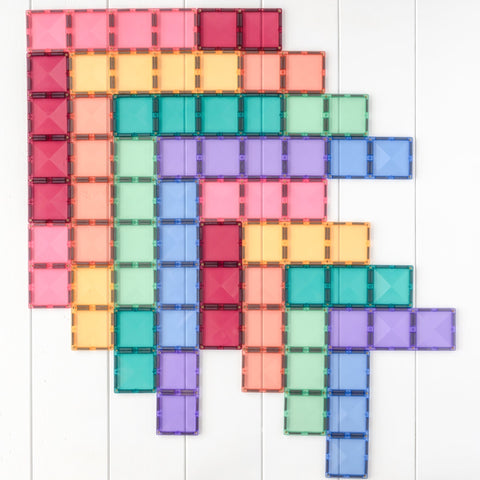 A collection of colorful Connetix shapes arranged in overlapping rectangular patterns on a white wooden surface. The tiles, from the Connetix Pastel Rectangle Pack 24pc, feature strong magnets and come in various pastel colors including red, pink, orange, yellow, green, blue, and purple. They create visually appealing geometric designs that are perfect for STEAM learning.