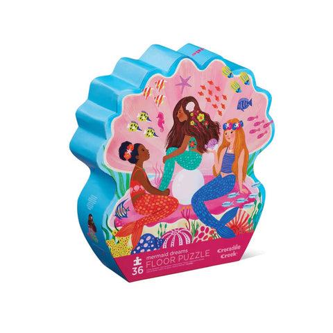 A whimsically illustrated, brightly colored shell-shaped box showcases three mermaids holding hands, surrounded by fish and underwater plants. Inside, it contains Crocodile Creek's popular "36pc Floor Puzzle - Mermaid Dreams.