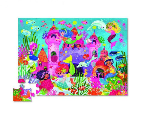 The Crocodile Creek 36pc Floor Puzzle - Mermaid Palace by Crocodile Creek illustrates an underwater scene teeming with colorful mermaids, sea creatures, and a vibrant coral reef. The mermaids are depicted playing and interacting with fish around a whimsical underwater castle. One piece is set aside, and the puzzle comes in a sturdy storage box.