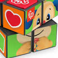 A close-up image of the colorful, partially twisted Fisher-Price Laugh & Learn Puppy's Activity Cube features various images on its sides, including a red heart, the "fp" logo, and parts of a cartoon character's face and hands holding a multicolored object – perfect for toddlers.