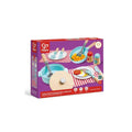 The HAPE Cook & Serve Set box showcases images of toy pots, pans, cutlery, a chopping board, food items, and a checkered tablemat on a purple background. This child toy kitchen accessory set from HAPE is perfect for children aged 2 to 8 years.