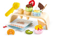 Introducing the HAPE Creamy Dreamy Ice Cream Corner, a vibrant wooden ice cream set from HAPE that includes cones, scoops, fruit slices, and other delightful toppings displayed on a compact wooden stand. Featuring realistic elements such as a yellow toy ice cream scoop, a menu, and various wooden fruit pieces, this set is perfect for imaginative pretend play.