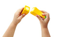 Two small hands hold separate pieces of a yellow broken object against a white background. The pieces feature magnetic ends, indicating they are part of the HAPE Farm Shop Fruit Playset by HAPE. This toy helps develop fine motor skills while ensuring safe and imaginative play.