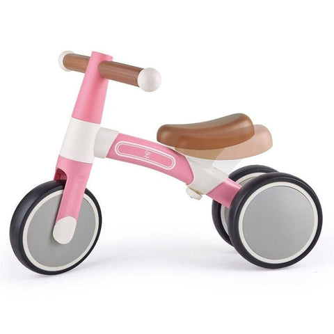 The HAPE My First Balance Bike Pink by HAPE is a pink and white adjustable balance bike designed for young children. It features a sturdy frame made from lightweight aluminium alloy, two large front wheels and two smaller rear wheels for added stability, and a brown, ergonomic seat. The handlebars and wheels are designed in a minimalist style.