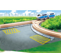 A blue and white toy train travels on wooden tracks through greenery with a cityscape in the background. The tracks, part of the Hape Adjustable Switch Track 2pc set by HAPE, curve over a paved road marked with yellow pedestrian lines, blending into a vibrant setting under a clear sky with a few clouds—a perfect toy for kids.