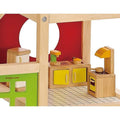 The Hape All Season Doll House Furnished by HAPE features a colorful wooden kitchen set. The four-room ensemble boasts a stove with an orange range hood, a sink adorned with yellow cabinets, a refrigerator, and a counter complete with drawers. The backdrop is decorated with red and green panels featuring geometric cutouts and includes moveable stairs for enhanced play possibilities.