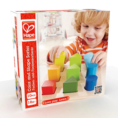 A box of the Hape Color and Shape Sorter toy is shown. The front of the box features a picture of a child engaging in color and shape identification with colorful geometric pieces that fit into corresponding holes on a wooden board. The box indicates it contains 10 pieces and is suitable for ages 18 months and up.