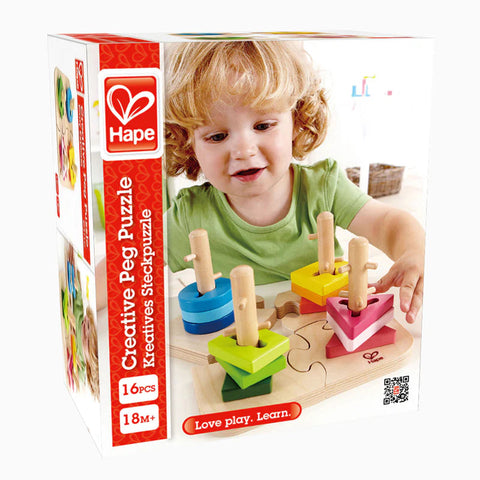 A young child with curly blond hair is playing with the Hape Creative Peg Puzzle from Hape. The colorful puzzle set includes vibrant wooden pegs in triangular, square, and circular shapes, designed to enhance fine motor skills and problem solving. The text on the box reads "16 pcs," "18M+," and "Love play. Learn.