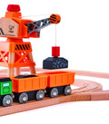 The Hape Diesel Freight Train by Hape is a wooden toy railroad set featuring a green and orange diesel freight train with two orange cargo cars. Nearby, an orange crane with a gray arm lifts a black cargo piece above the wooden track, all set against a white background.