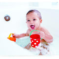 A baby sits in a bathtub filled with bubbles, smiling happily. The baby enjoys water play, holding the Hape Happy Buckets Set – a red and white polka dot bucket in one hand and an orange and yellow toy from Hape in the other, making bath time delightful.