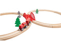 A Hape Play Essentials Classic Figure 8 Set features a classic figure-eight wooden toy train layout with a red train on the tracks. The set, by Hape, includes a red bridge, several green trees, and a traffic sign with a railroad crossing symbol, offering the ultimate railway experience for any young conductor.