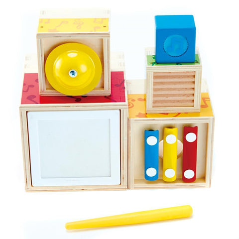 The Hape Stacking Music set by Hape is a wooden children's musical toy featuring colorful percussion instruments. It includes a yellow bell, blue cube, white frame, three small xylophone bars in red, yellow, and blue, and a yellow mallet. All parts are mounted on or stored in wooden blocks for easy stacking.