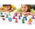 Two children, a boy and a girl, are engaged in play-based learning with Hey Clay 15 Pack - Animals figurines on a table. The boy is holding a small blue ball while the girl clutches a pink one, both smiling and focused on their colorful Hey Clay creations from the brand's collection.