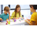 Three children are sitting at a white table in a brightly lit room, immersed in a creative activity with the Hey Clay 15 pack - Animals modeling clay by Hey Clay. One boy wears a teal shirt, another boy is dressed in yellow, and a girl is outfitted in green. Various colorful animal-shaped clay creations are scattered on the table, making play-based learning fun and engaging.