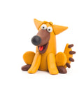 A whimsical clay figurine of a yellow dog with exaggerated features, including a large black nose, wide eyes, and a red tongue sticking out, is depicted against a white background. This playful piece from the "Hey Clay 15 Pack - Animals" by Hey Clay is perfect for enthusiasts or play-based learning activities and boasts a charmingly cartoonish appeal.