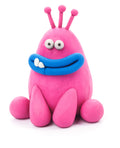 A playful, egg-shaped modeling clay creature from the Hey Clay 6 pack - Monsters set by Hey Clay, featuring a pink body with googly eyes, a wide blue smile showcasing a single tooth, and three antennae-like appendages on its head. It has round feet and is positioned on a white background, exuding a cartoonish and whimsical charm that makes it perfect for play-based learning.