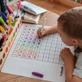 A child drawing on the Hey Doodle Silicone Activity Mat - 100 Squares (Large) with markers.