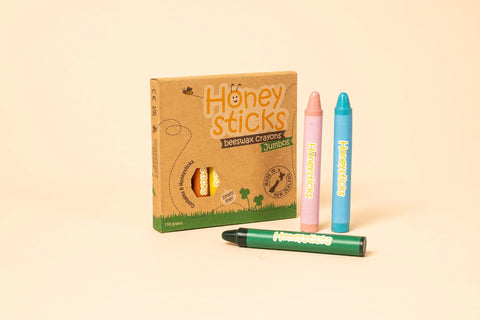 A box of Honeysticks Beeswax Crayons Jumbo (8pk) is displayed alongside three jumbo crayons in pink, blue, and green colors, each labeled with the Honeysticks logo. These natural, non-toxic crayons are set against a solid light beige background.