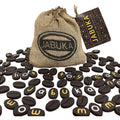 A burlap sack labeled "Jabuka" is surrounded by scattered coffee-bean-shaped pieces. The tiles feature letters in yellow and white, arranged to spell words such as "Jabuka," "toy," "shop," and "mom." A tag on the sack reads "Jabuka - Twisting Letter Word Game: Totally Twisted Fun!"—a word game with a twist!