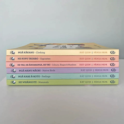 A stack of six bilingual board books with colorful spines arranged horizontally, featuring titles in both Māori and English by Kat Quin. The topics include clothing, opposites, colors and shapes, native birds (from the "Kuwi Ngā Manu Māori - Native Birds Board Book"), feelings, and mammals. They are authored under the KUWI THE KIWI brand and encourage readers to Save the Kiwi.