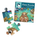 The Kuwi's Rowdy Crowd Floor Puzzle - 24 Large Pieces from KUWI THE KIWI is shown. The box showcases Kuwi the Kiwi, a charming character from a beloved children's book, holding a magnifying glass beside other animals. Three puzzle pieces with parts of the same illustration are displayed next to the box. This eco-friendly puzzle is designed for children ages 3 and up.