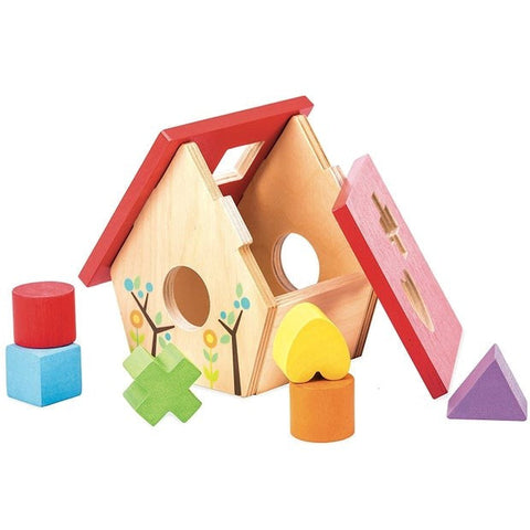 The Le Toy Van Little Bird House Shape Sorter by LE TOY VAN is a sustainable wood toy that resembles a birdhouse with a red roof and charming tree and leaf designs. It includes various colorful wooden shapes, such as a red cylinder, blue cube, green cross, yellow heart, orange cylinder, and purple triangle, which are placed around it to enhance pre-reading skills.