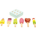 The Le Toy Van Set of Lollies by LE TOY VAN is a wooden children's toy set that includes various wooden ice lollies in vibrant designs. Each lolly features a distinct shape and pattern, such as stripes, swirls, and sprinkles. The set also comes with a light blue box with small holes to keep the ice lollies upright.