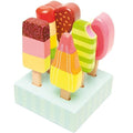 The Le Toy Van Set of Lollies from LE TOY VAN includes colorful wooden toy popsicles in various shapes and patterns, mounted on a light blue rectangular display stand. These wooden ice lollies feature vibrant colors such as pink, yellow, green, and orange with designs resembling sprinkles, stripes, and layers.