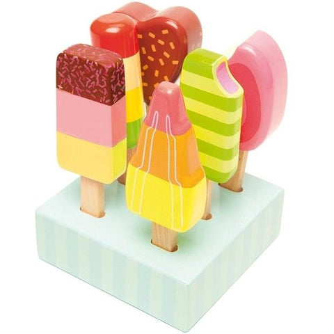 The Le Toy Van Set of Lollies from LE TOY VAN includes colorful wooden toy popsicles in various shapes and patterns, mounted on a light blue rectangular display stand. These wooden ice lollies feature vibrant colors such as pink, yellow, green, and orange with designs resembling sprinkles, stripes, and layers.