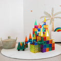 A vibrant structure made up of transparent Learn & Grow Rainbow Magnetic Tiles Ball Run Pack 88pc is set up on a round white mat. The tiles come in various shapes such as squares, triangles, and rectangles. To the left sits a wicker basket, and in the background is a wall featuring an illustration of a palm tree.