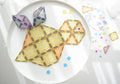 A flat-lay image showcases a mosaic toy turtle crafted from interlocking geometric tiles on a white circular surface. The turtle, made using the Magblox Pastel Pack 66pc by Magblox, features a mix of yellow and orange tiles for its body, purple tiles for its fins, and has one googly eye. Small colorful circles and tiles are scattered around.