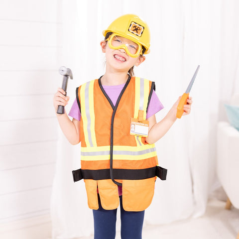 A smiling child wearing the Melissa & Doug Construction Worker Role Play Costume Set, complete with a yellow hard hat and safety vest, holds plastic tools—a toy hammer in one hand and a toy screwdriver in the other. Dressed in a light purple shirt and blue pants, the child stands indoors against a white background, completing their adorable construction worker costume from Melissa & Doug.