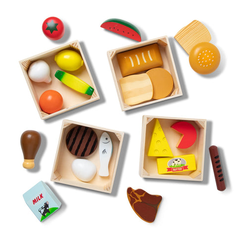 Four wooden crates are filled with toy food items from the five food groups, including a tomato, onion, milk carton, fish, cheese, steak, bread, butter, egg, chicken drumstick, chocolate bar, watermelon slice, and lemon wedge. The "Melissa & Doug Food Groups" set by Melissa & Doug is neatly arranged on a white background.