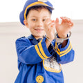 A young boy dressed in the Melissa & Doug Police Officer Costume Role Play Set from Melissa & Doug smiles at the camera. He playfully holds up his wrists, showing toy handcuffs around them. The costume, featuring yellow stripes and a badge, is complete with a machine-washable jacket and a walkie-talkie with sound effects.