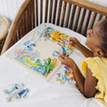 A young child wearing a yellow sleeveless top is sitting on a white bed, assembling the Melissa & Doug Wooden Jigsaw Puzzle - Under The Sea 24pc on a wooden frame. The kids' puzzle from Melissa & Doug includes various sea creatures like fish, seahorses, and octopuses. Some pieces are still scattered around.