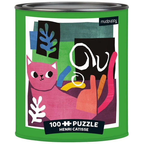 A cylindrical green paint can tin from Mudpuppy features an illustration inspired by Henri Matisse, depicting a pink cat surrounded by colorful abstract shapes and leaves. The text on the can reads "Artsy Cats Puzzle: 100-piece Henri Catisse.