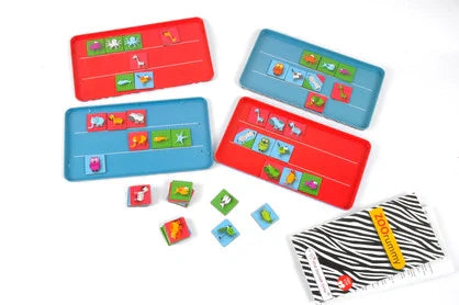 Four game boards (two red, two blue) and several animal-themed tiles laid out on a white surface. The animal tiles feature various creatures, including elephants, lions, and birds. A zebra-patterned instruction booklet labeled "Purple Cow Travel Game - Zoo Rummy" is also shown, perfect for road trips in its travel game tin box.