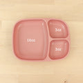 The Re-Play Divided Tray by REPLAY, a pink three-sectioned plate crafted from recycled material, is shown on a wooden surface. The left section is labeled "16 oz," while each of the two smaller sections on the right is labeled "3 oz." This eco-friendly tray exemplifies durable tableware ideal for mindful dining.