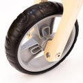 Close-up of a Runna Mini - Gumtree children's balance bike wheel. The black wheel, with its thick tread, features a sturdy grey hub. The light wooden bike frame from RUNNA, shown here with a single screw attaching the frame to the wheel, is perfect for toddlers learning to ride on balance bikes.