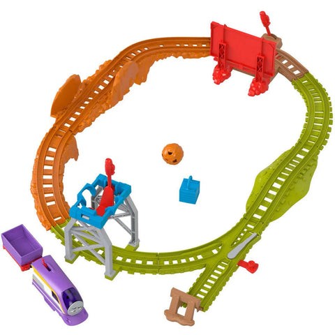 The Fisher-Price Thomas & Friends Motorized Engine - Round & Round Kana toy train set features interconnected tracks in vibrant orange, green, and brown sections. Included in the set is a purple train with a red cargo cart, along with a blue crane equipped with a hook. Additionally, it comes with various accessories like signs, a blue box, and a round orange object. Perfect for fans of motorized train sets!