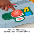 A child's hand pushes a large red button marked with a white "T" on the gray Fisher-Price Thomas & Friends Talking Cranky Delivery Train Set. The toy features additional buttons, such as a yellow musical note and blue gear, offering over 325 songs, sounds, and character phrases.