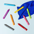 Eight colorful Tiger Tribe Bath Crayons by TIGER TRIBE, ideal for fostering creative play, are scattered on a light blue surface alongside a blue piece of cloth. These bath crayons, perfect for developing fine motor skills, come in shades of blue, yellow, pink, orange, green, gray, red, and light green.